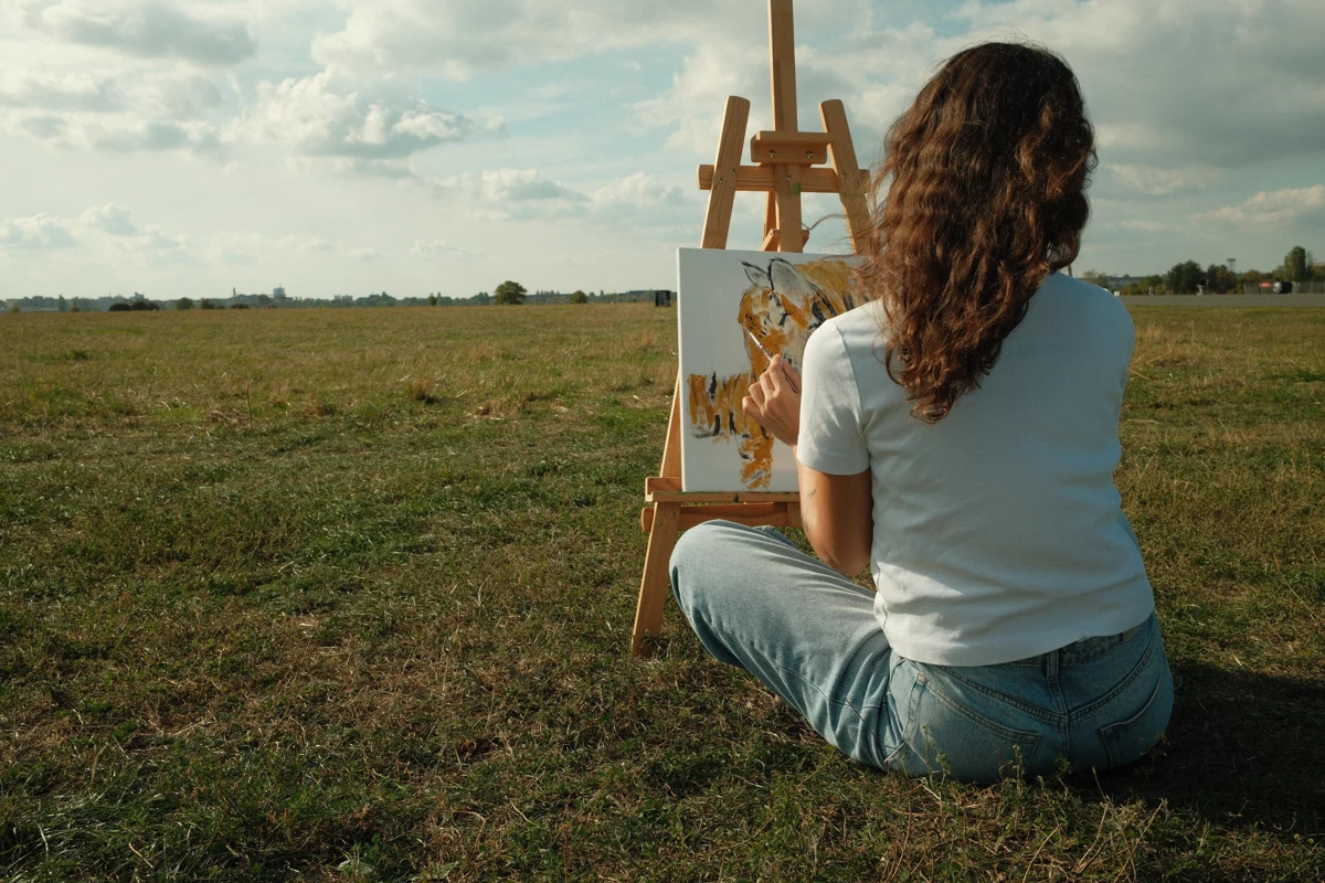 Benan seated outdoors, seen from behind while painting at her easel